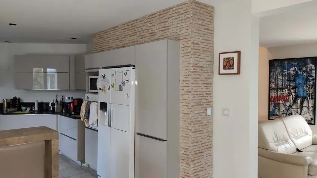 Cuisine moderne avec des placards blancs, un mur carrelé beige et un agencement ouvert.