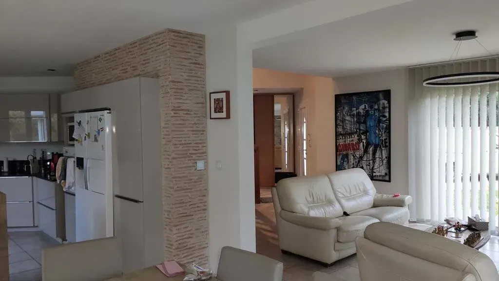 Vue intérieure d'une maison moderne avec une cuisine, un salon, des meubles blancs et un tableau au mur.