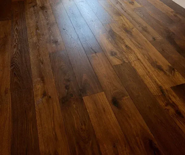 Plancher en bois dur brun foncé, vue en biais, montrant le grain du bois et quelques reflets de lumière.