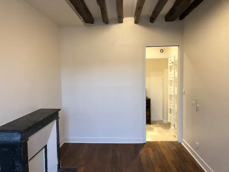 Pièce vide avec une cheminée, des poutres apparentes, une porte et un parquet.