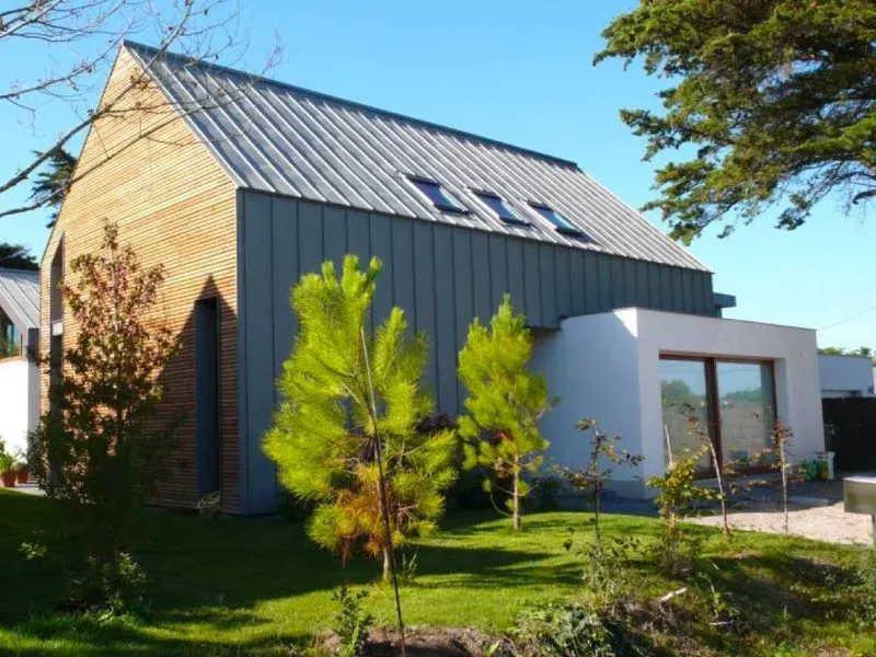 Maison moderne avec un toit en métal et une façade en briques blanches. Pelouse et arbres.