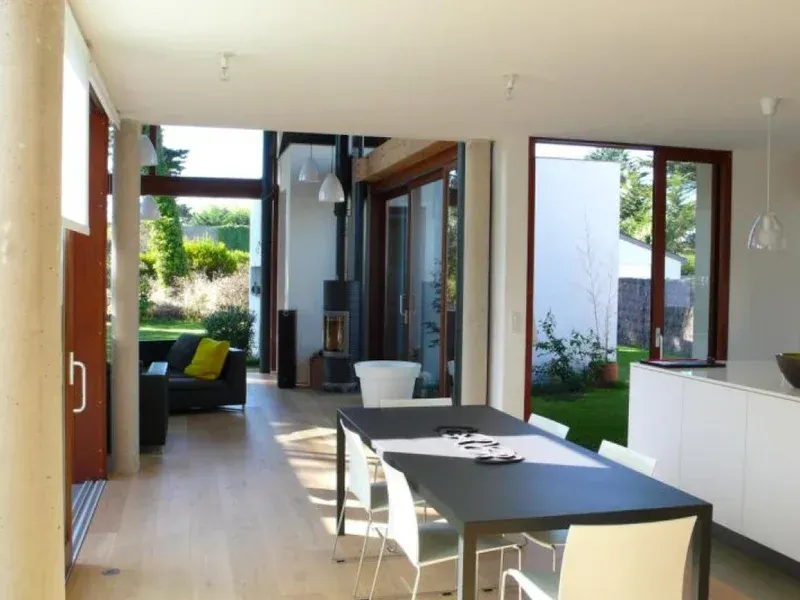 Coin repas avec une table noire et des chaises blanches, donnant sur un jardin par des portes coulissantes en verre.