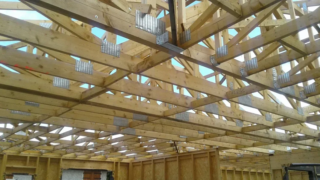 Charpente de toit en bois dans un bâtiment inachevé, avec des plaques de connexion métalliques.