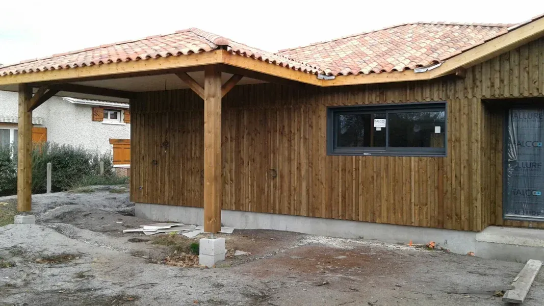 Cabane en bois avec un toit de tuiles et un abri voiture. Les murs sont bruns.