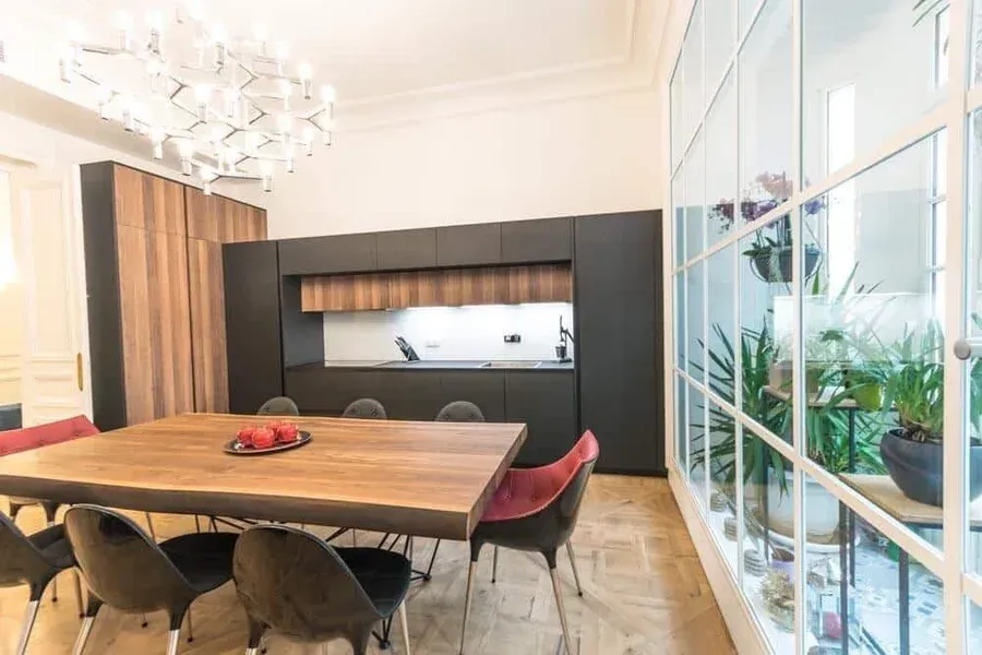 Salle à manger avec table en bois, des chaises noires, de cuisine, de paroi vitrée et des plantes décoratives.