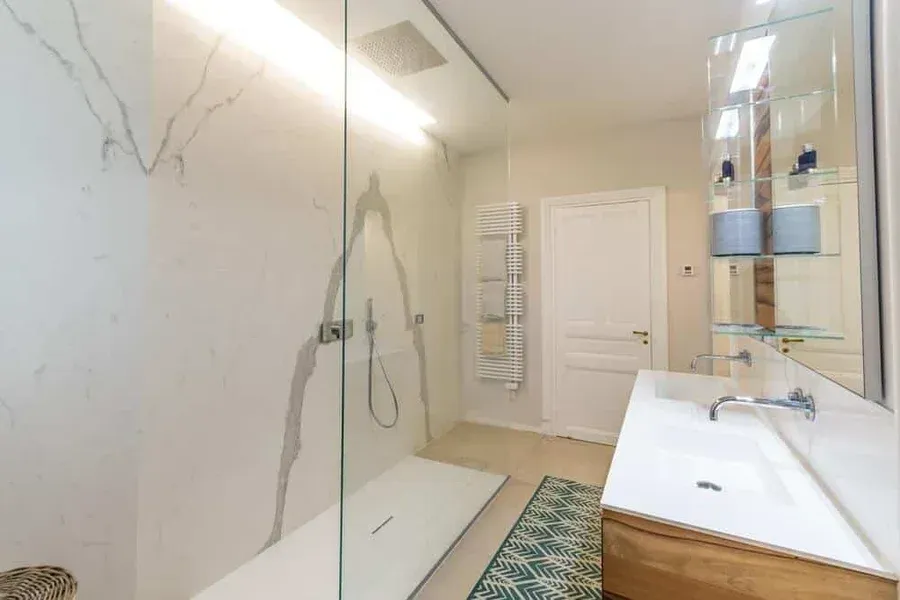 Salle de bains moderne avec une douche en marbre blanc, un meuble lavabo et une porte en verre.