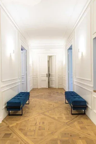 Couloir avec deux bancs bleus, des murs blancs et un parquet.