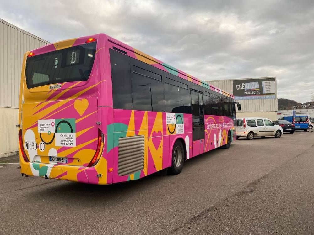 Bus urbain rose et jaune garé sur un parking par temps couvert
