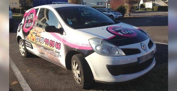 Voiture compacte blanche avec des visuels publicitaires roses, garée dans une rue, vue de face