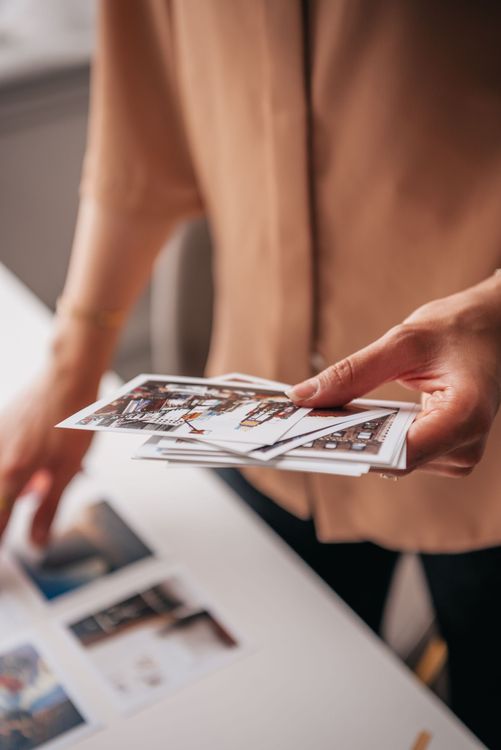 Personne tenant des photos imprimées au-dessus d’une table sur laquelle sont éparpillés des tirages photo