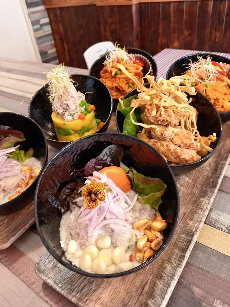 Tazones de comida peruana sobre una tabla de madera: ceviche, pollo frito, verduras y guarnición.