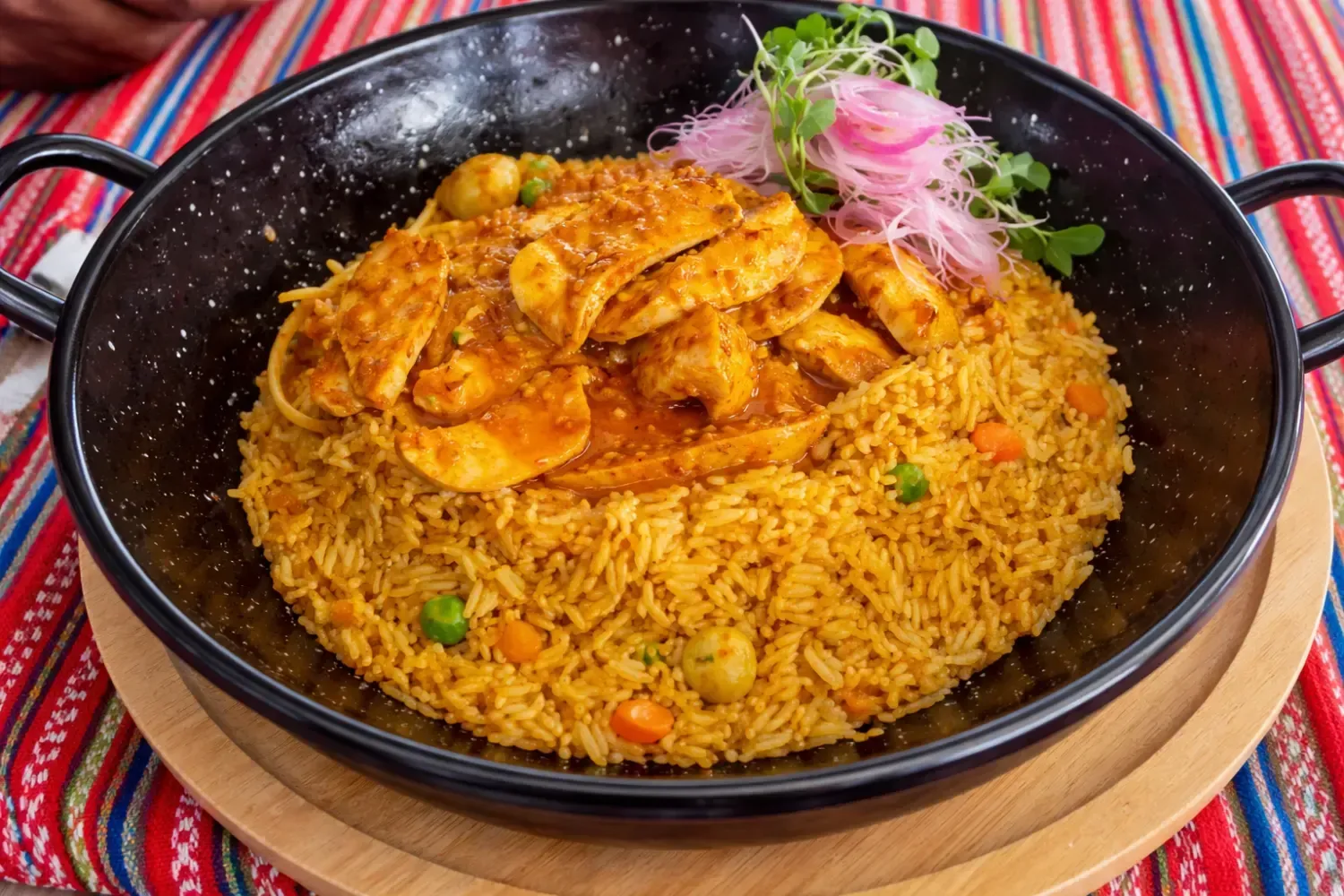 Plato de pollo y arroz servido en sartén negra, adornado con verduras y encurtidos.