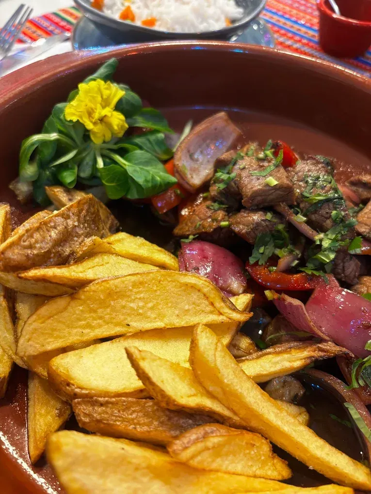 Salteado de carne con papas fritas y arroz. Cebolla roja, hierbas verdes y una guarnición de flores amarillas.