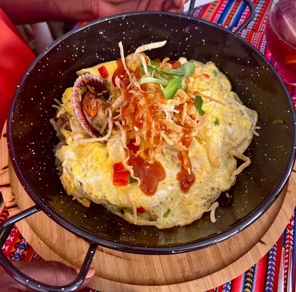 Plato de pollo y arroz servido en sartén negra, adornado con verduras y encurtidos.