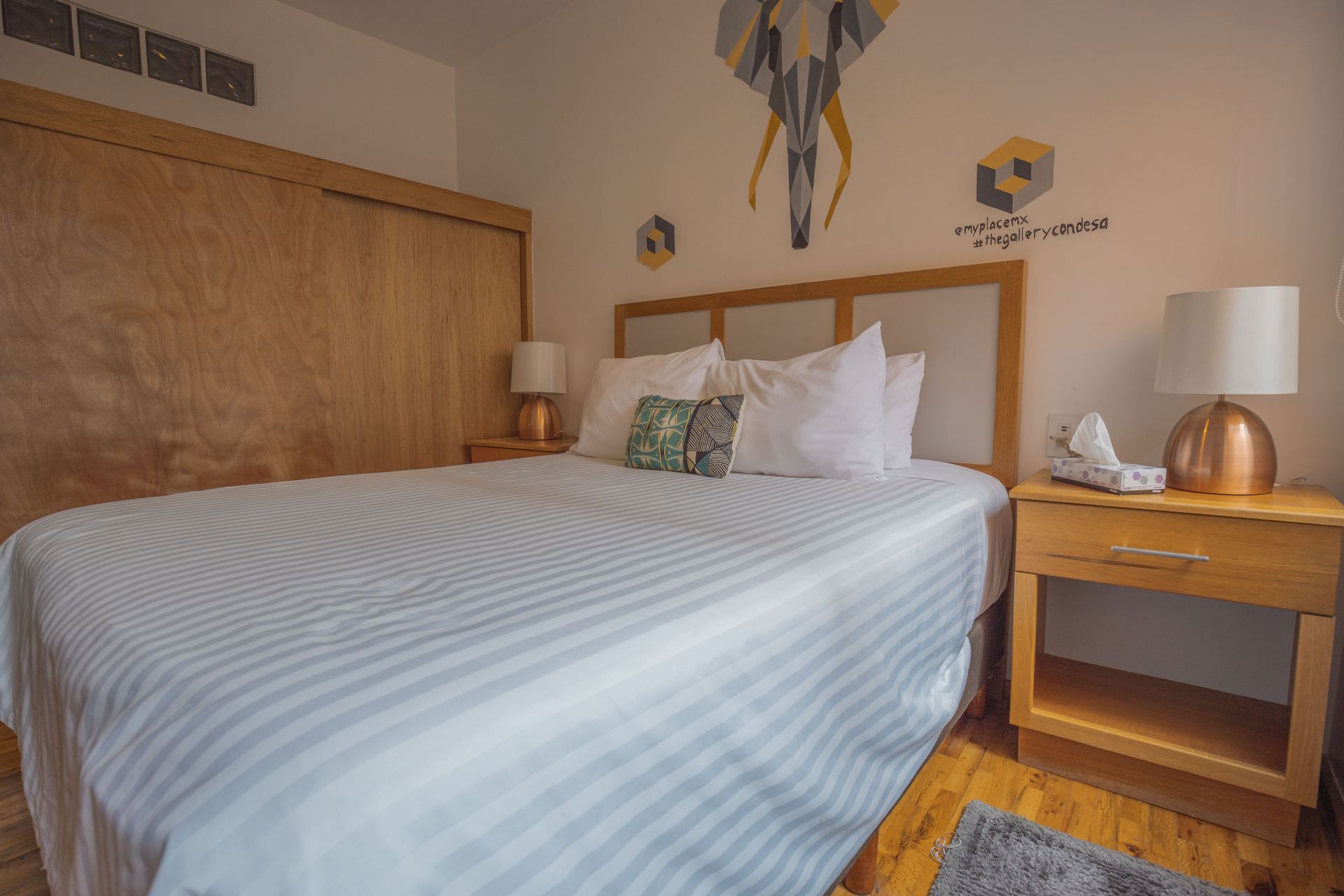 A bedroom with a bed , nightstand , lamps and a painting on the wall.