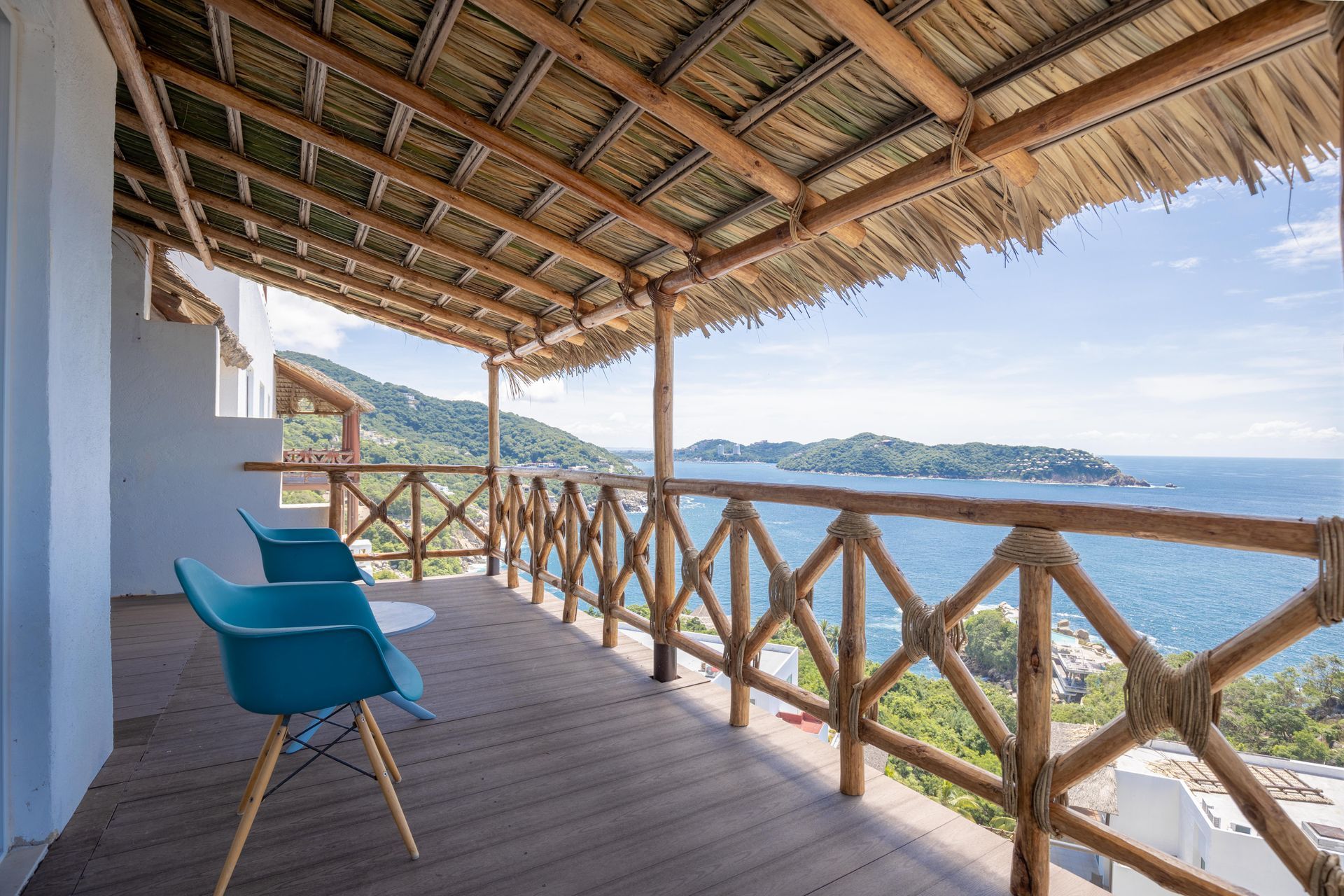 A balcony with chairs and a thatched roof overlooking the ocean.
