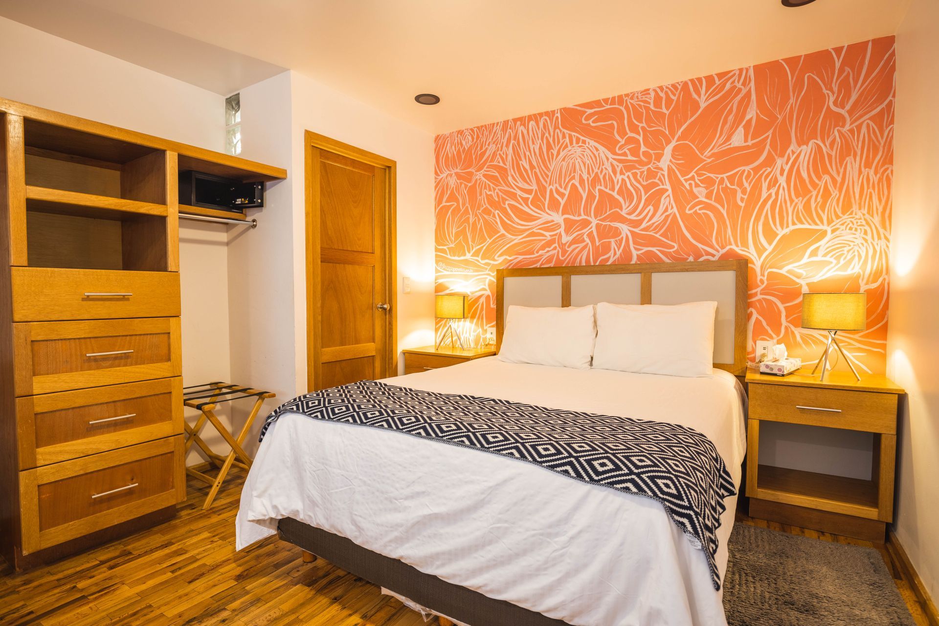 A hotel room with a bed , nightstands , dressers and a floral wall.