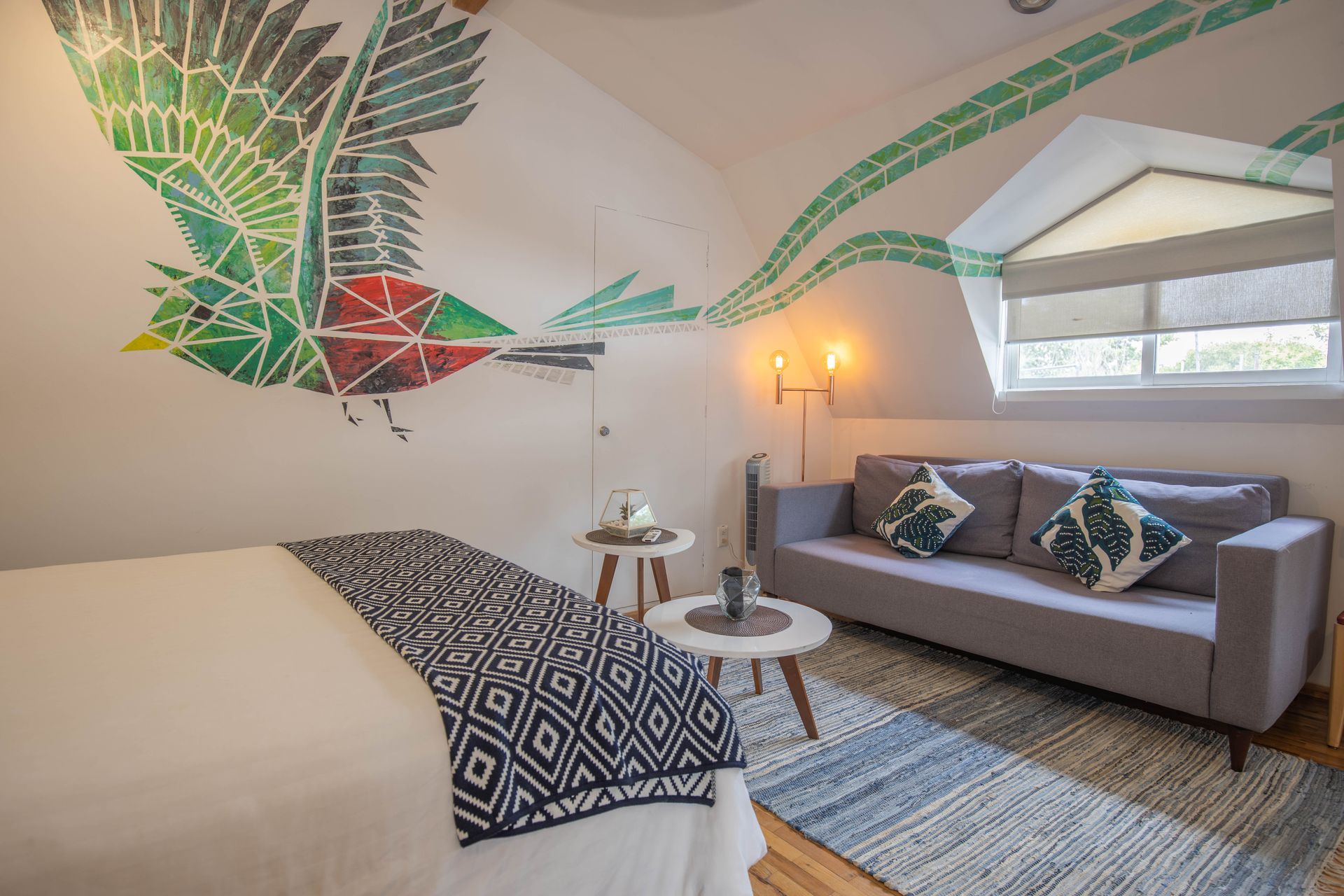 A bedroom with a couch and a bed with a bird painting on the wall.