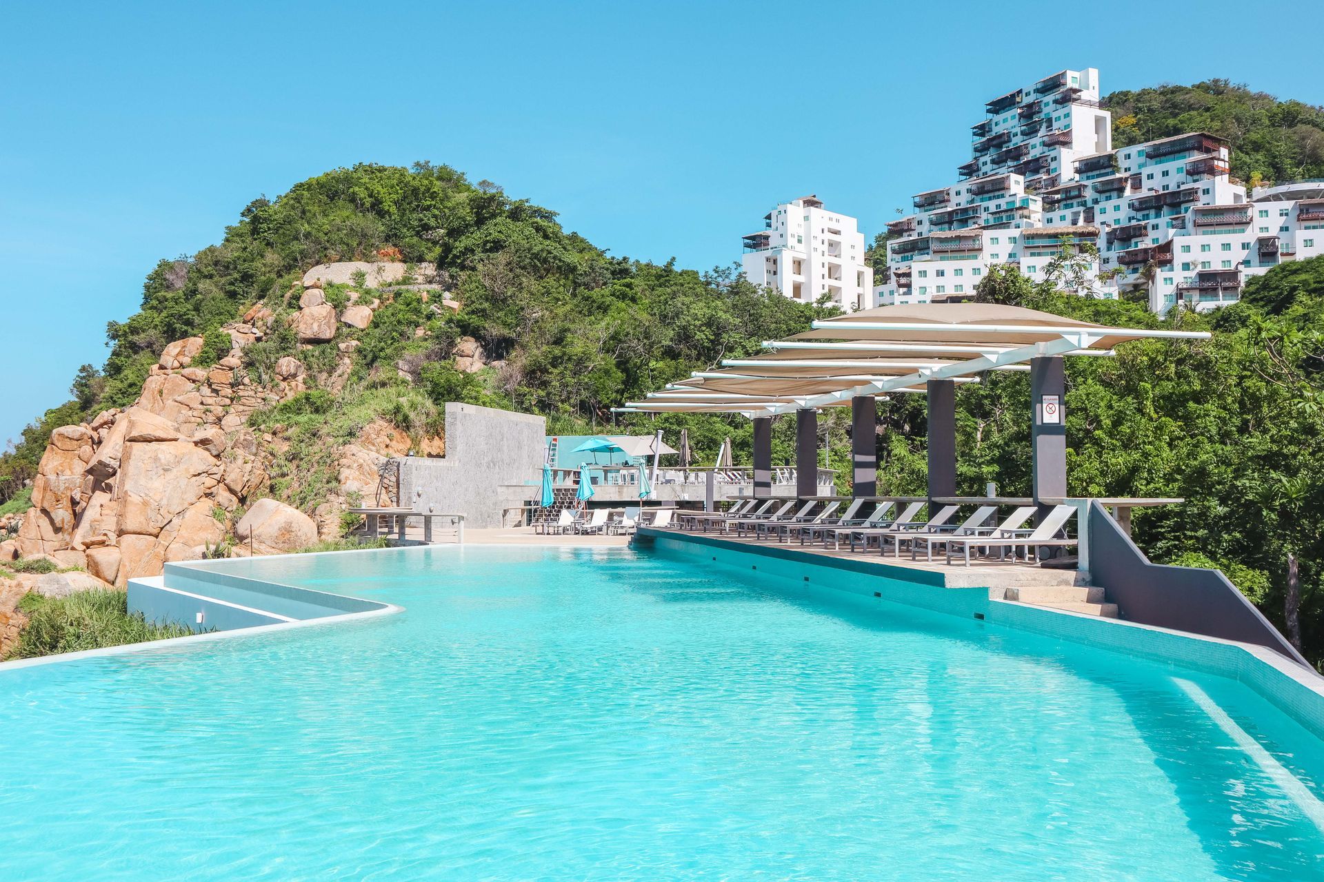 A large swimming pool surrounded by chairs and a mountain in the background.
