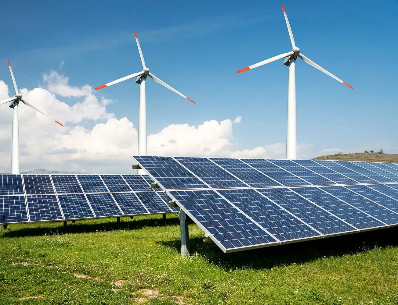 Paneles solares y turbinas eólicas en un campo de césped verde bajo un cielo azul.