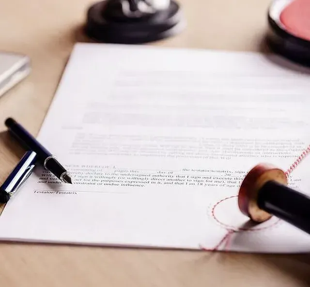 Un documento con un bolígrafo, un sello y una almohadilla de tinta sobre una superficie de madera, lo que sugiere que se está finalizando el papeleo oficial.