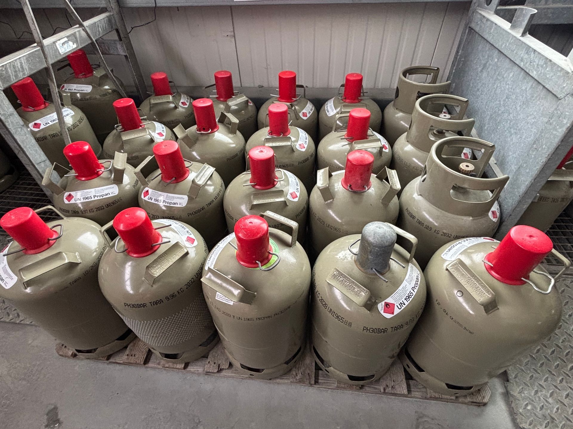 Eine Person mit Arbeitshandschuhen schließt einen Schlauch an einen blauen Kältemittelbehälter auf dem Boden an.