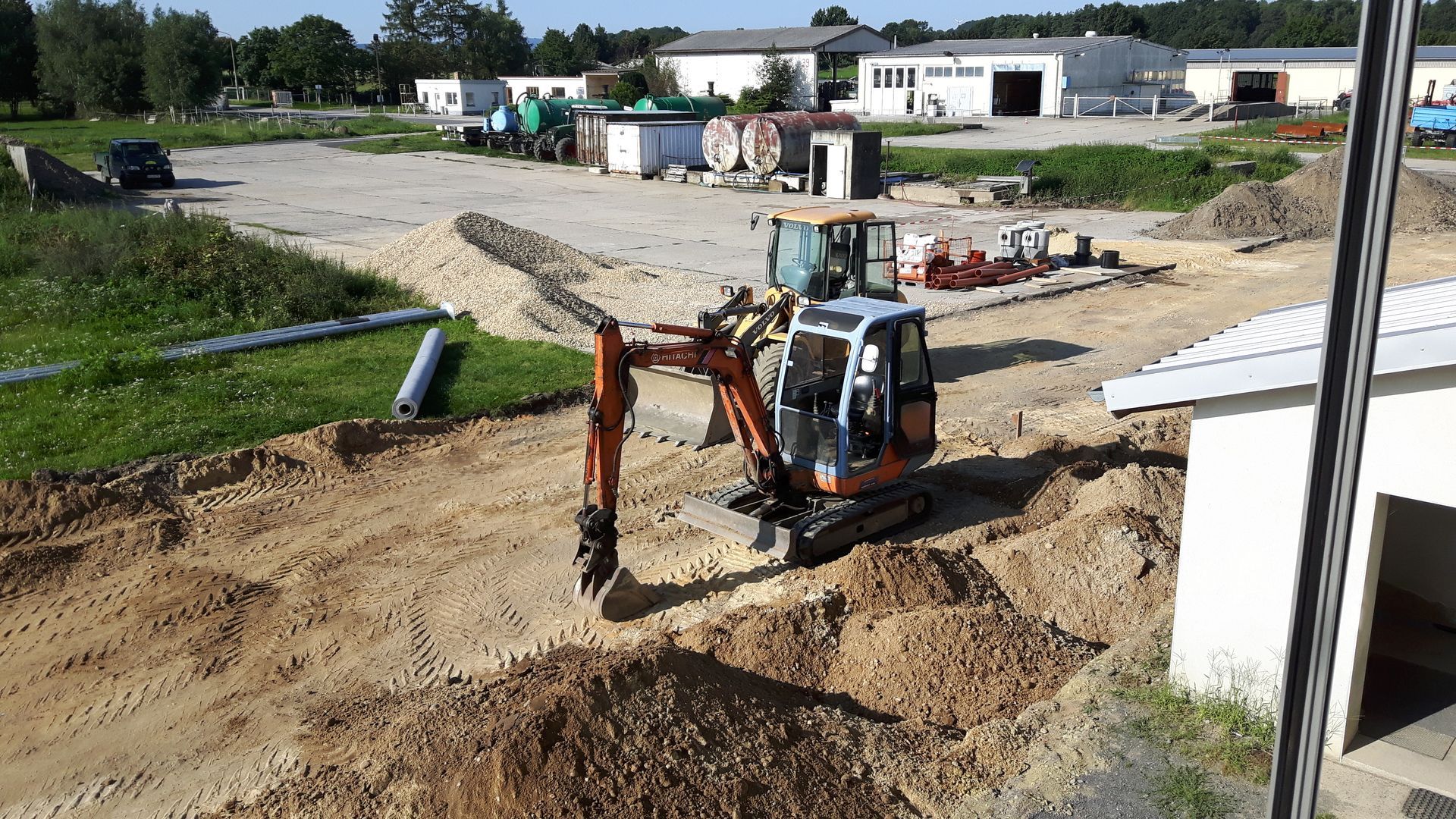 Außenaufnahme einer Baustelle mit einem Bagger bei Erdarbeiten auf dem Firmengelände.