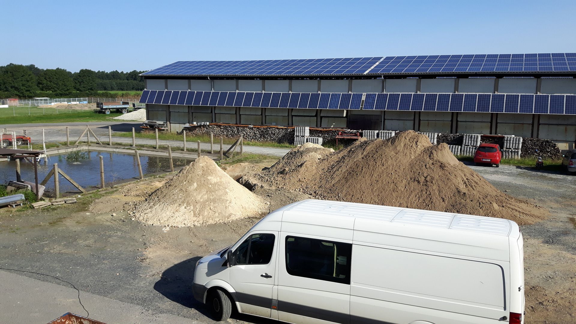 Weißer Transporter vor einem großen Stallgebäude mit Photovoltaikanlage.