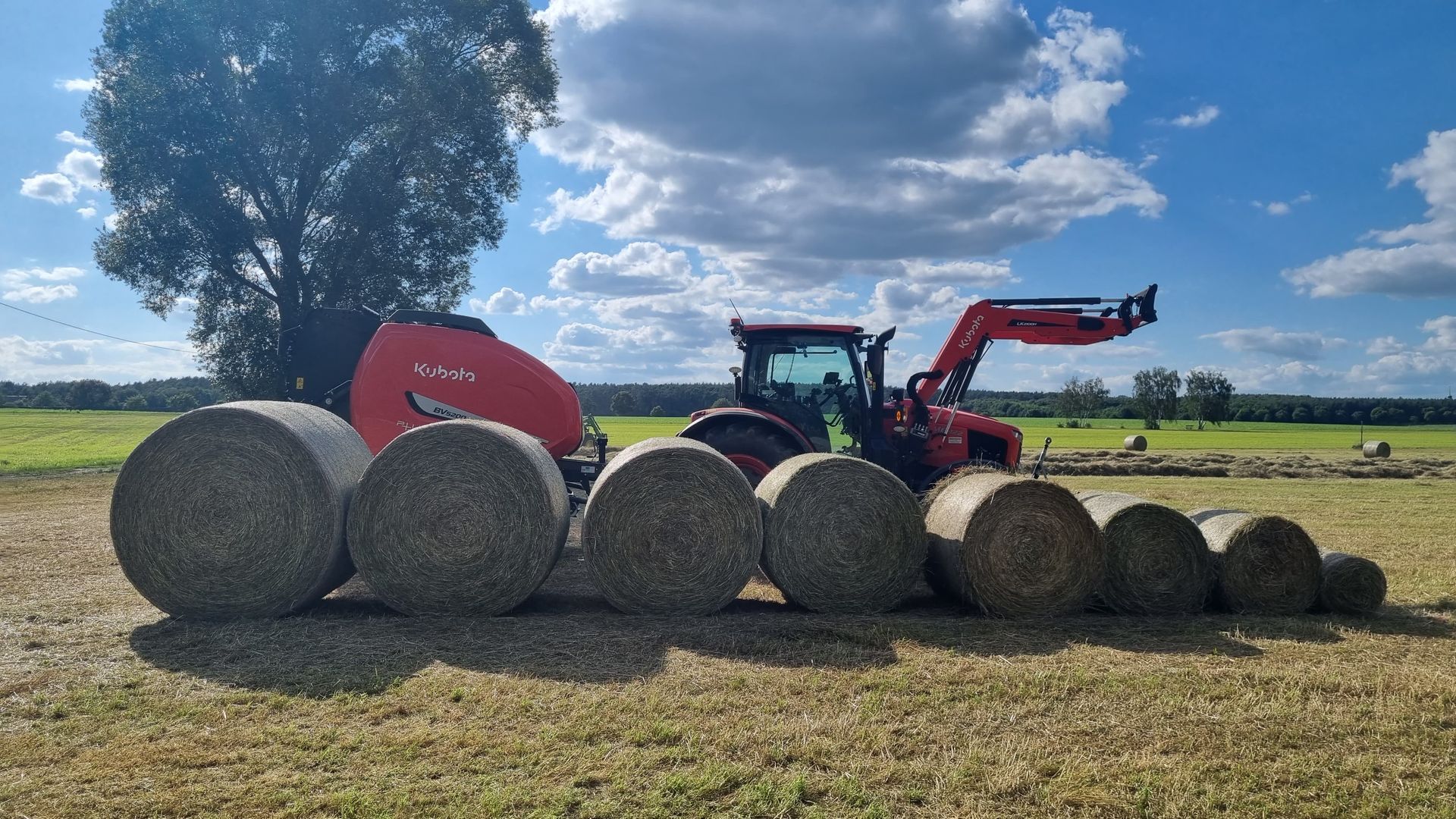 Traktor auf dem Feld neben einer Reihe Heuballen unterschiedlicher Größe.