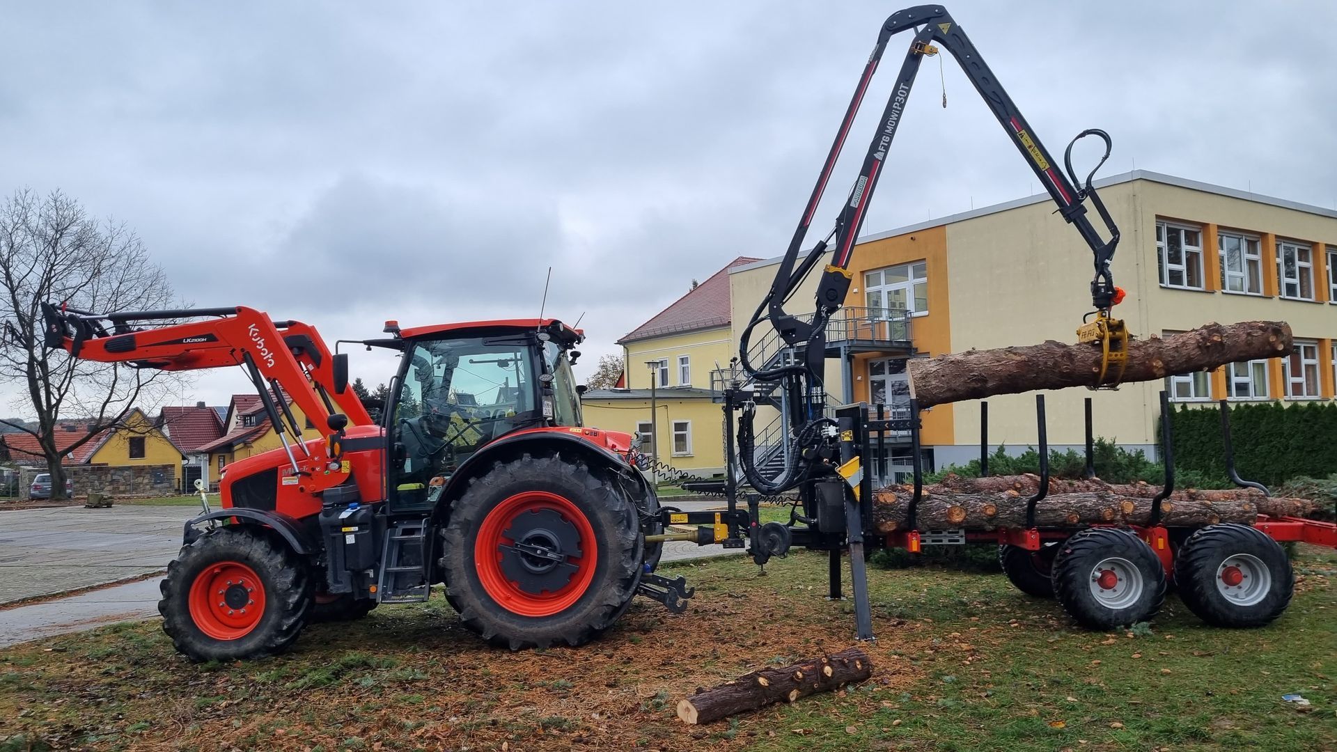 Traktor mit Forstkran-Anhänger beim Verladen von Baumstämmen.