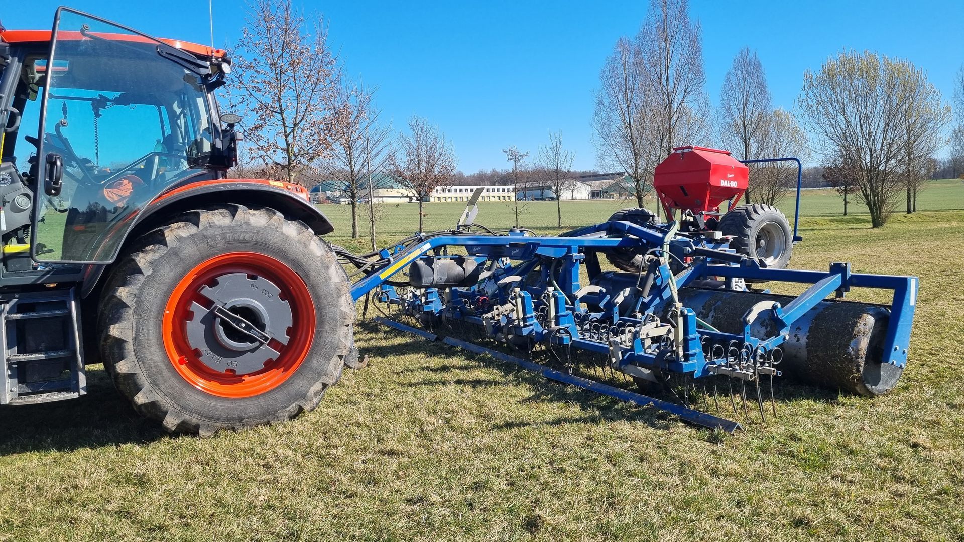 Roter Traktor mit angehängter Wiesenwalze und Direktsaatvorrichtung.