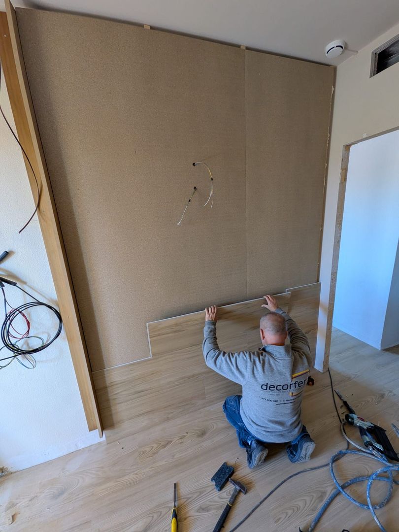 Un trabajador arrodillado sobre un suelo de madera instala tablones laminados con herramientas a mano.