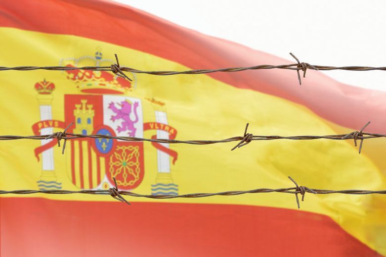 Una bandera española está detrás de un alambre de púas.