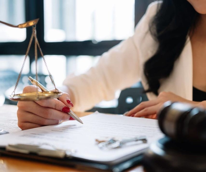 Una mujer está escribiendo en un trozo de papel con una balanza de la justicia en el fondo.