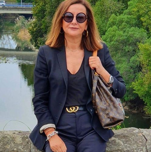 Una mujer que lleva gafas de sol y un traje negro está sentada en un puente con vistas a un río.