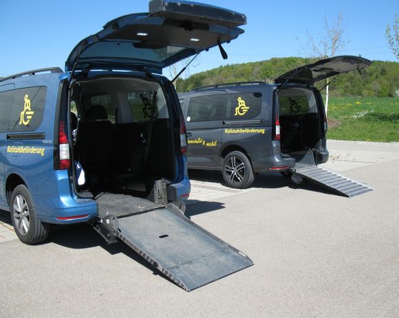Eine Pflegekraft schiebt eine Person in einem manuellen Rollstuhl eine Rampe hinauf in den Laderaum eines Fahrzeugs.