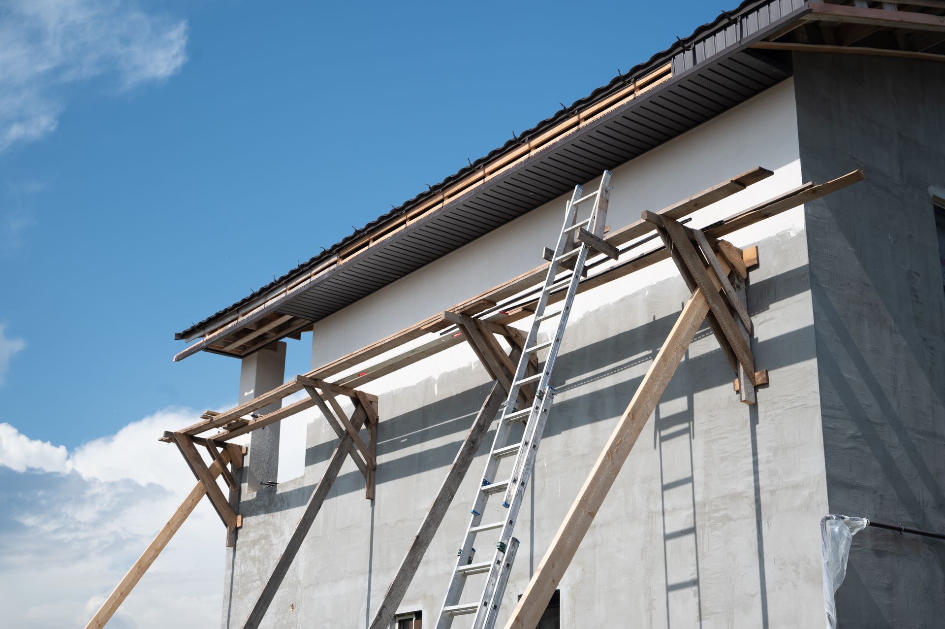 Des échelles appuyées contre une maison en construction, avec un débord de toit et des supports en bois.