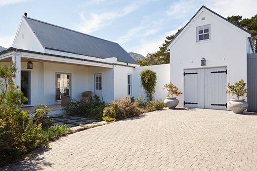Maison blanche avec garage indépendant, allée pavée, toit foncé et jardin paysager à l’avant, en plein soleil