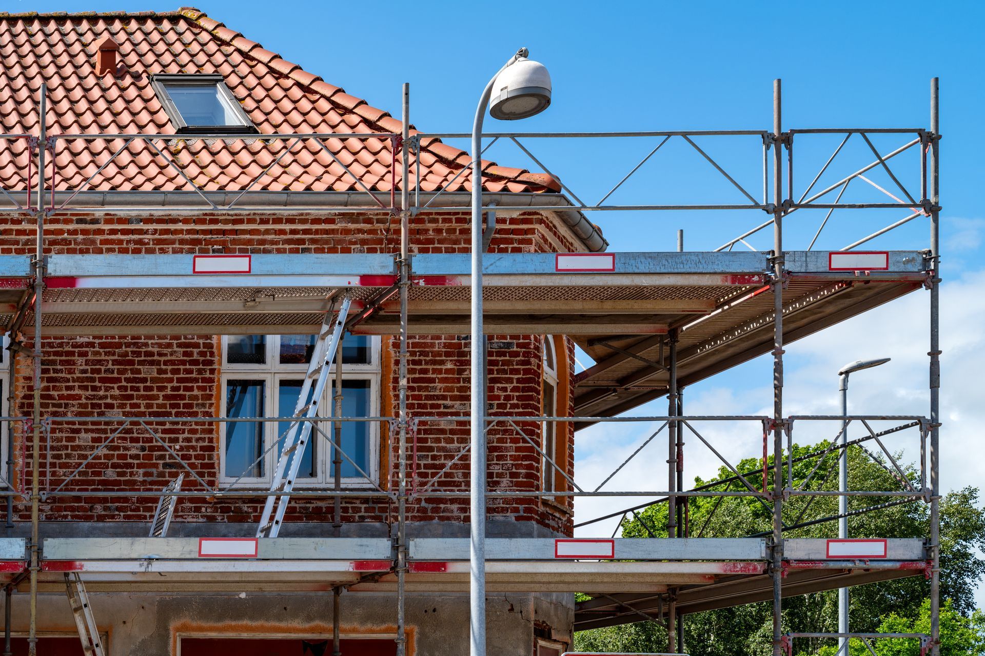 Maison en rénovation avec échafaudage, toit de tuiles rouges et lampadaire devant