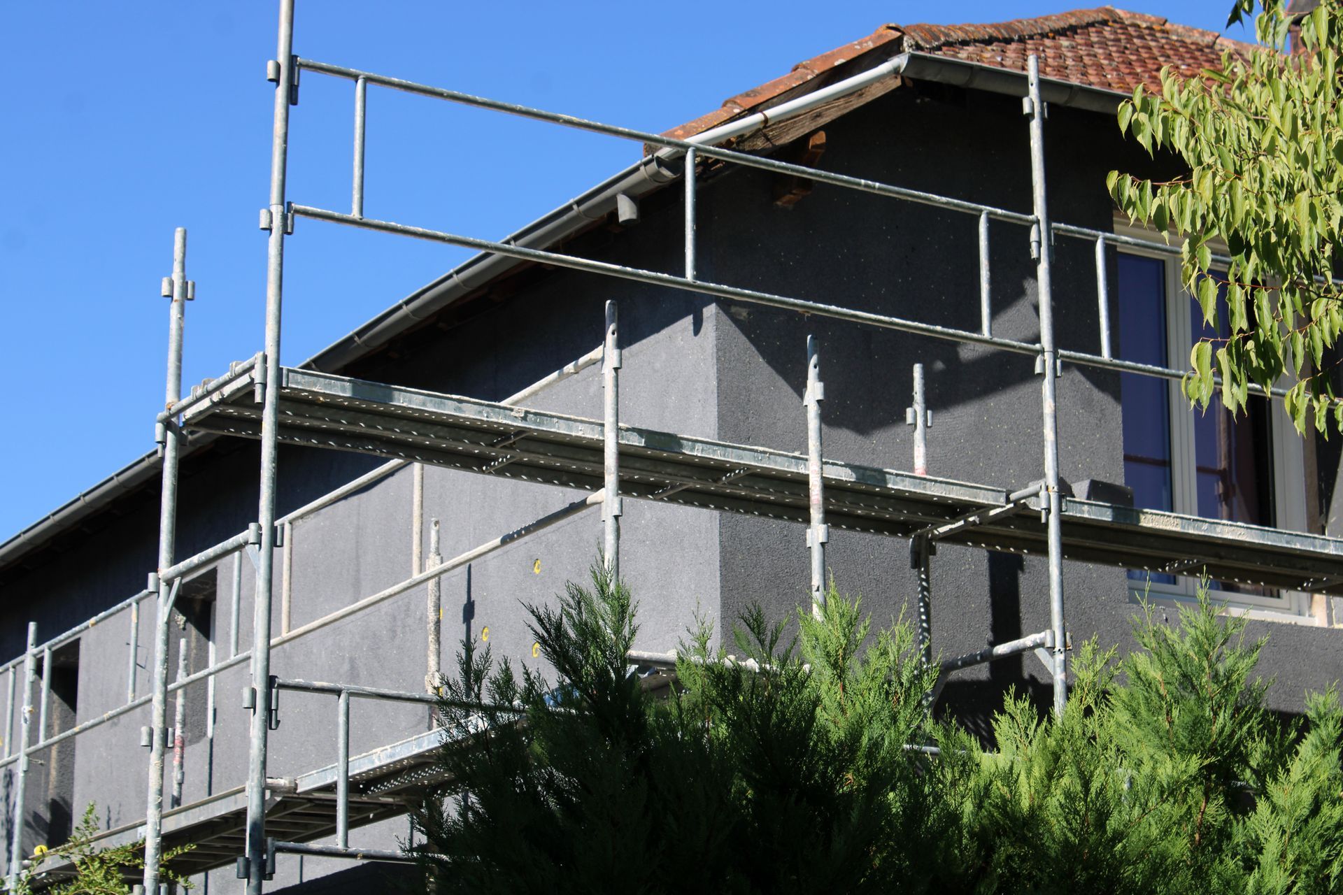 Maison en construction, avec un échafaudage, sur fond de ciel bleu et d’arbres au premier plan