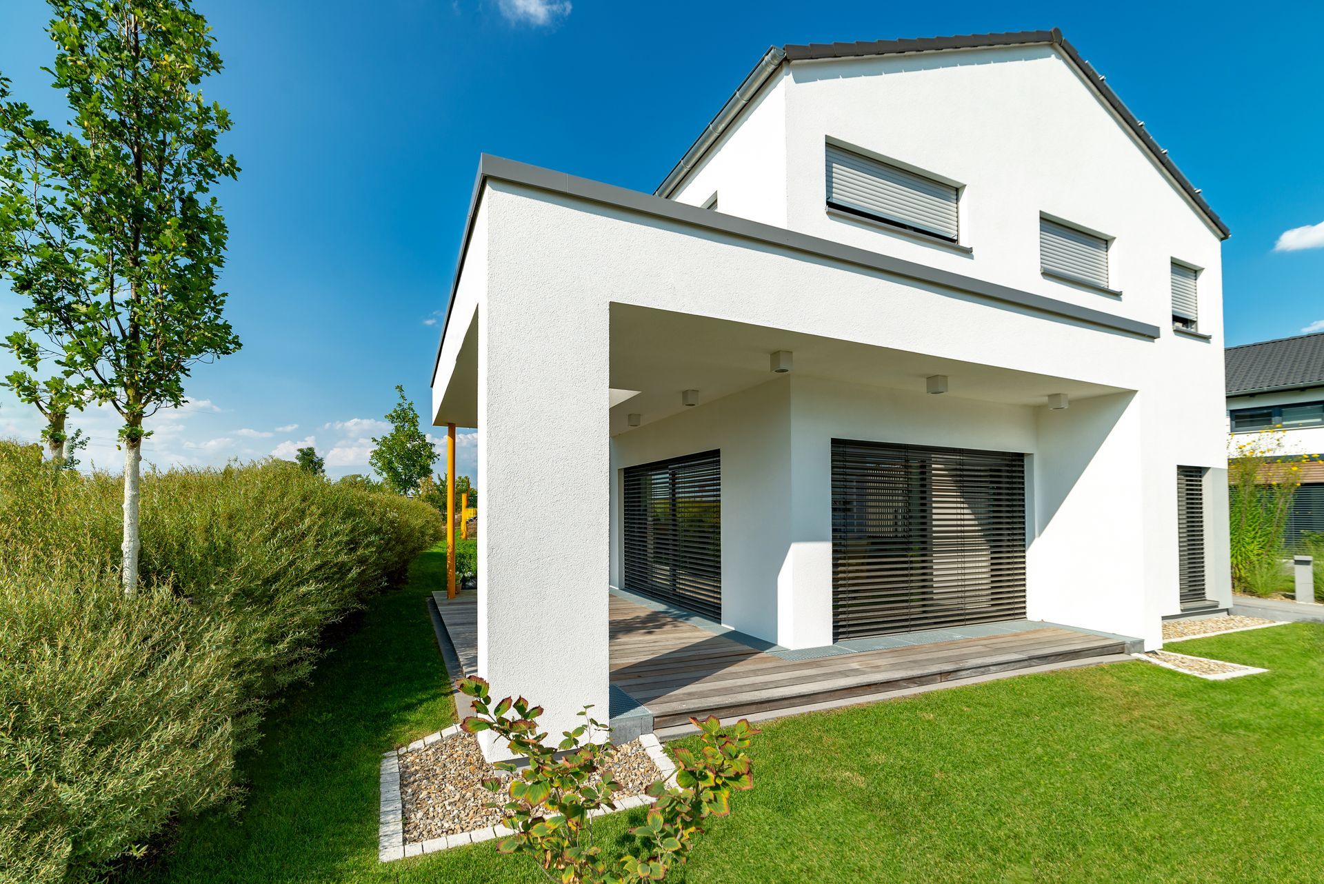 Extérieur moderne de maison blanche avec patio couvert, pelouse verte et ciel bleu