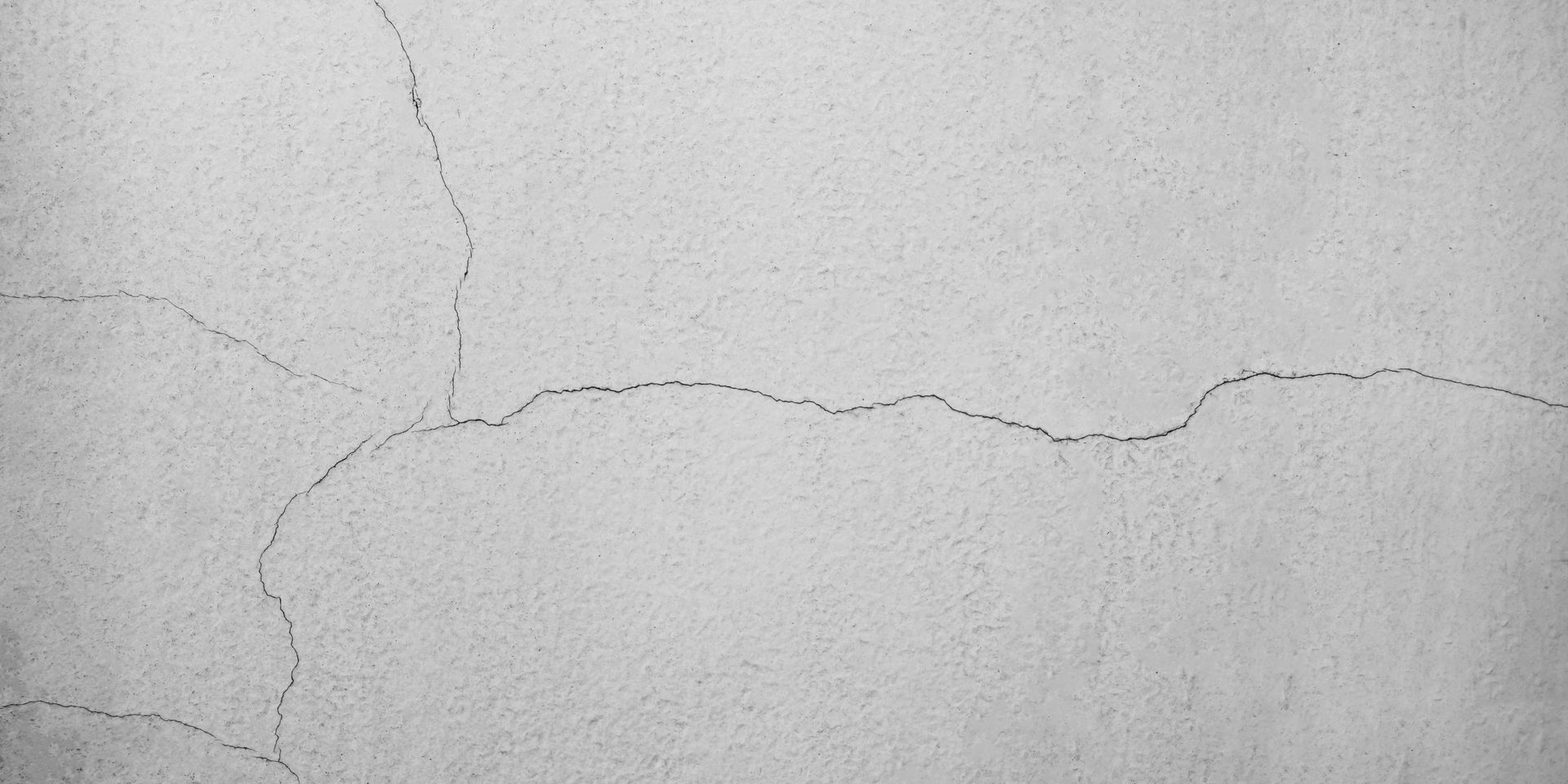 Gros plan d’un mur gris clair fissuré, avec une longue fissure horizontale.