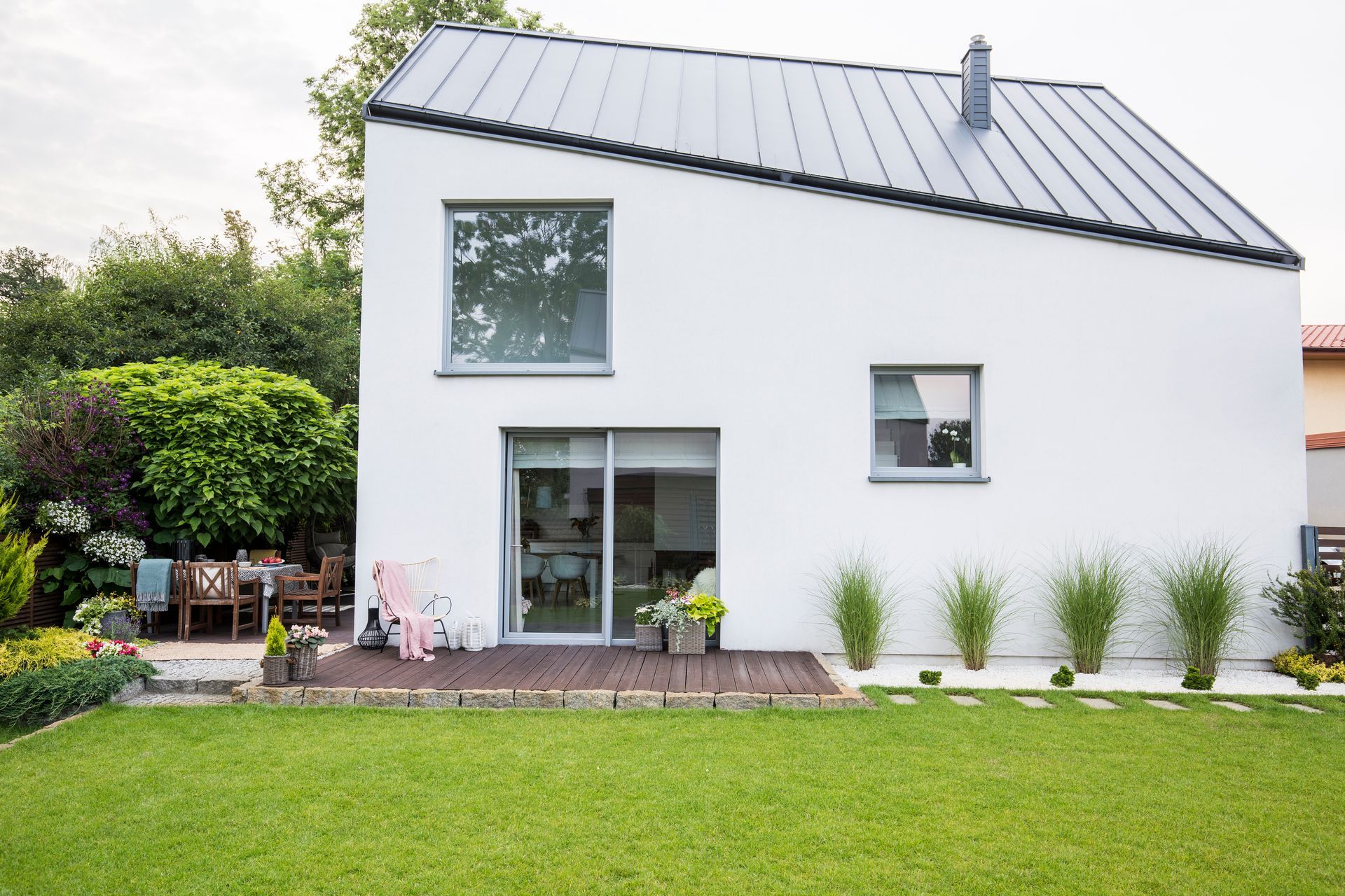 Maison moderne blanche avec un toit gris, une grande pelouse verte et des portes-fenêtres donnant sur l’avant.