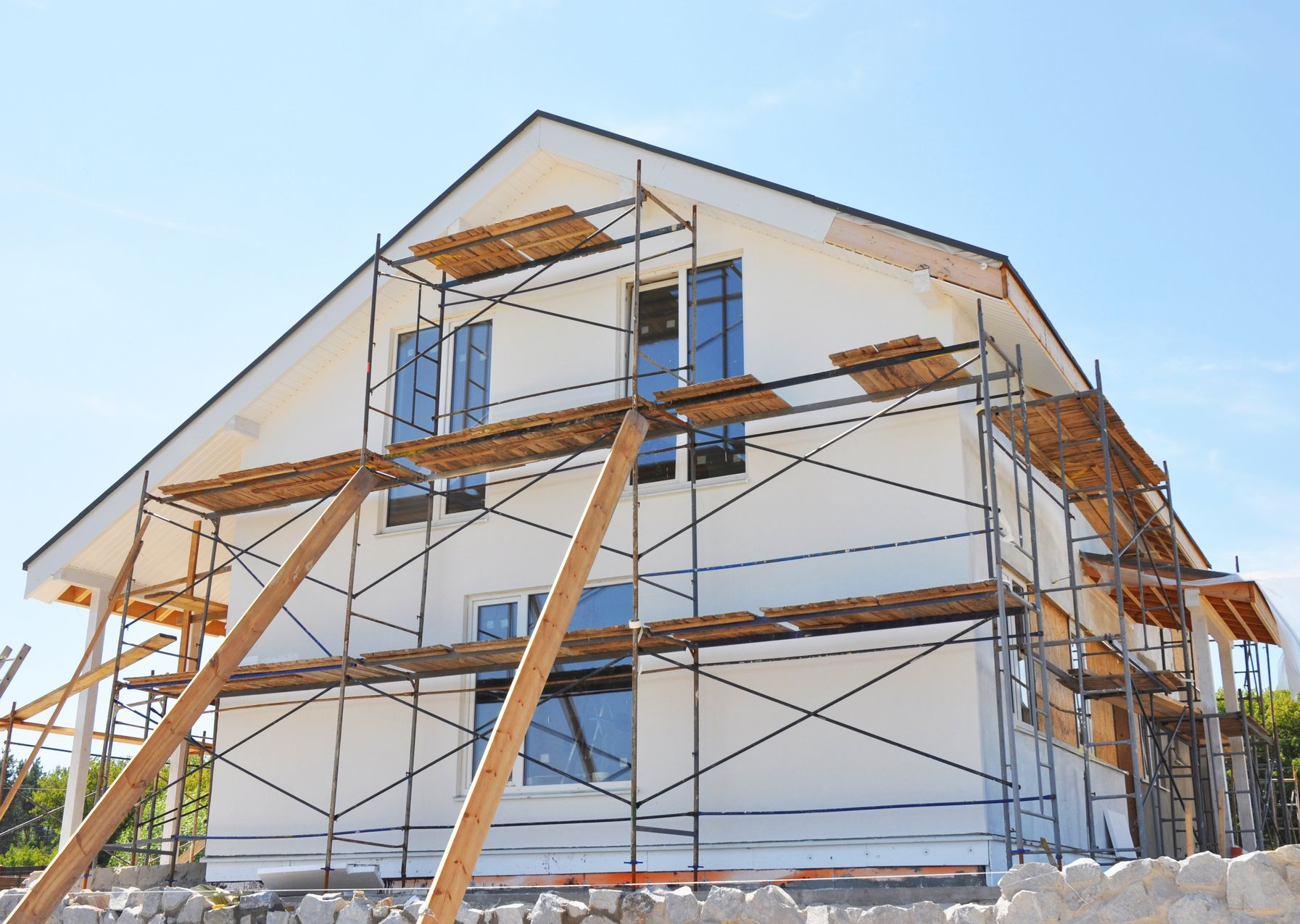 Maison en construction, avec des échafaudages et des étais en bois, sur fond de ciel bleu