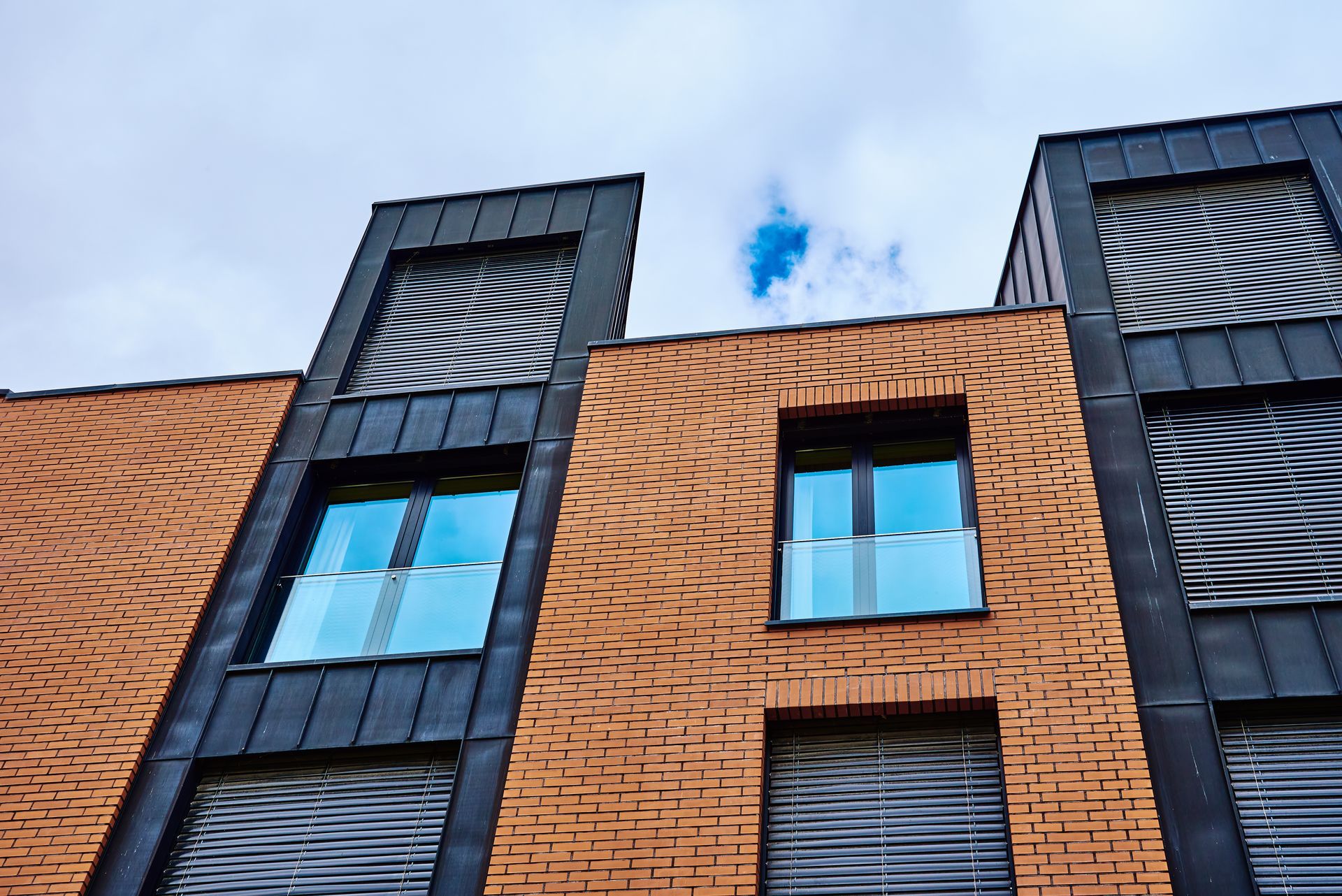 Façade d’un bâtiment en briques avec deux sections de fenêtres verticales foncées et un ciel bleu au-dessus