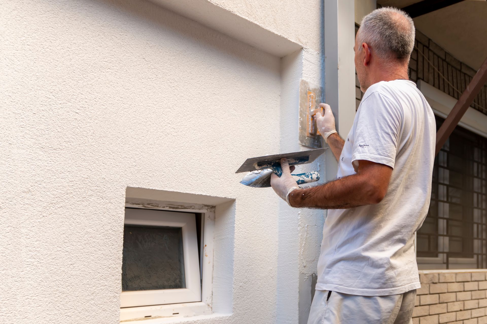 Un ouvrier applique du crépi sur un mur extérieur, à côté d’une petite fenêtre
