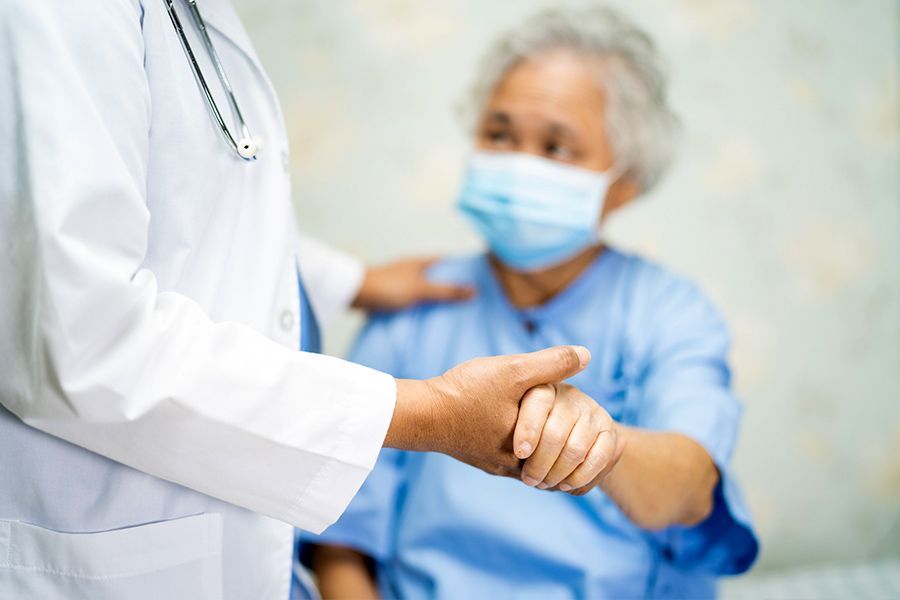 Un médico le estrecha la mano a un paciente anciano que lleva una mascarilla.