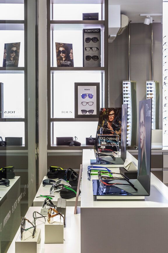 Interior de tienda de gafas con estantes, mesas de exhibición y gafas en exposición.
