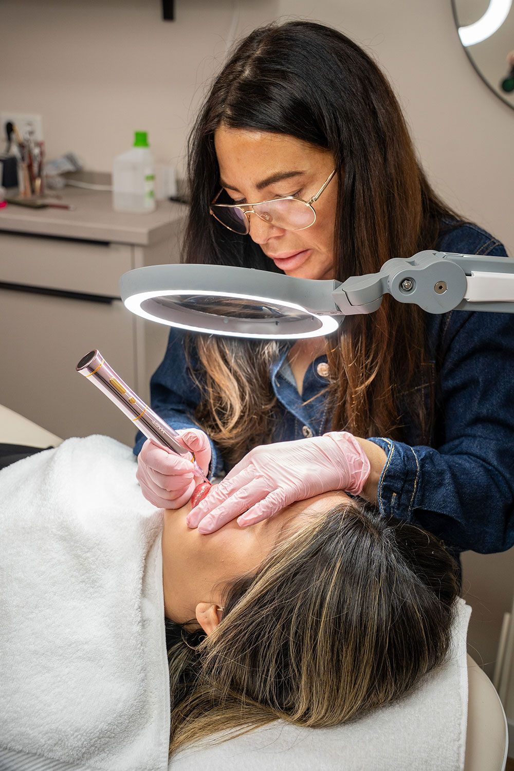 Eine Frau betrachtet mit einer Lupe das Gesicht einer anderen Frau.