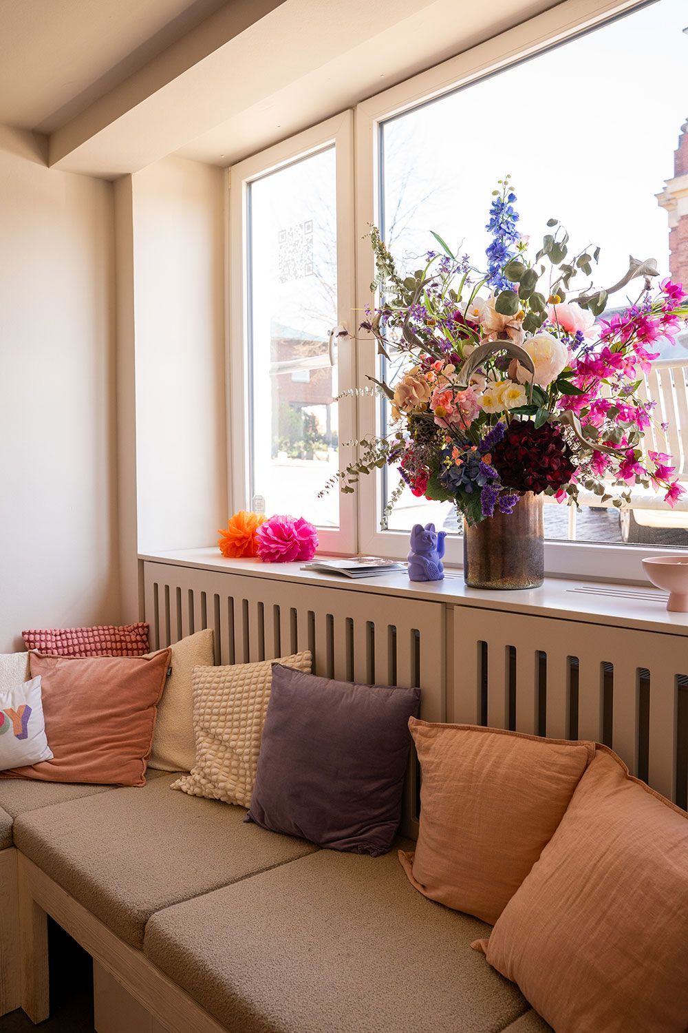 Ein Sofa mit Kissen und einer Vase mit Blumen auf einem Fensterbrett.